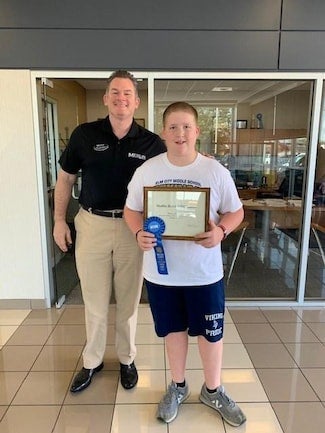 A boy holding an award plaque and blue ribbon with a man.