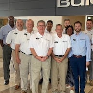 A large group of people in white polo shirts smiling together indoors