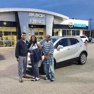 Three people standing outside a Buick GMC dealership next to a car.