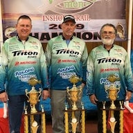 Three men in matching fishing jerseys holding trophies at a 2019 event.